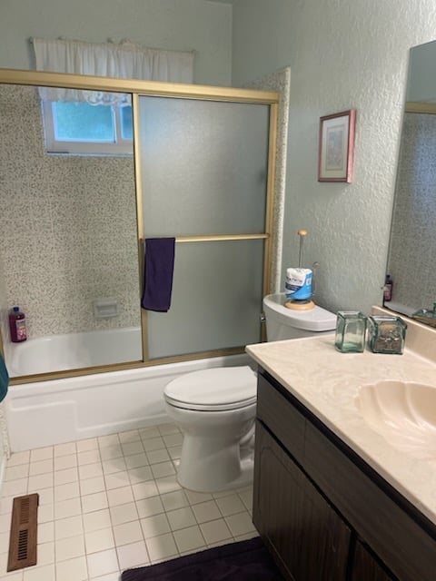 Bathroom interior with white tile floor, dark vanity with sink, toilet, and glass-door shower enclosure with gold trim