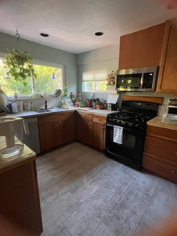 Kitchen with wood cabinets, black stove, light green walls, tile flooring, and window overlooking trees